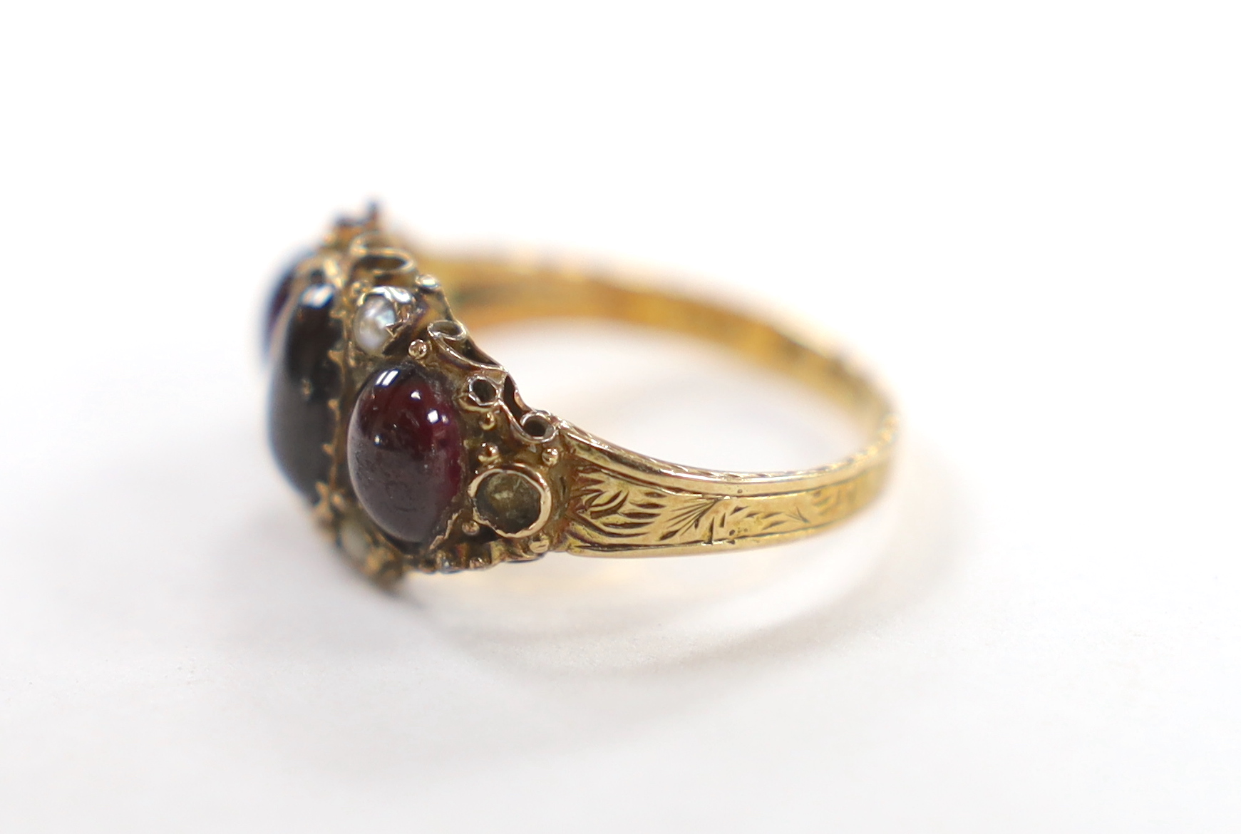 A Victorian 15ct gold, foil backed three stone cabochon garnet and seed pearl cluster set half hoop ring, size O, gross weight 3 grams.